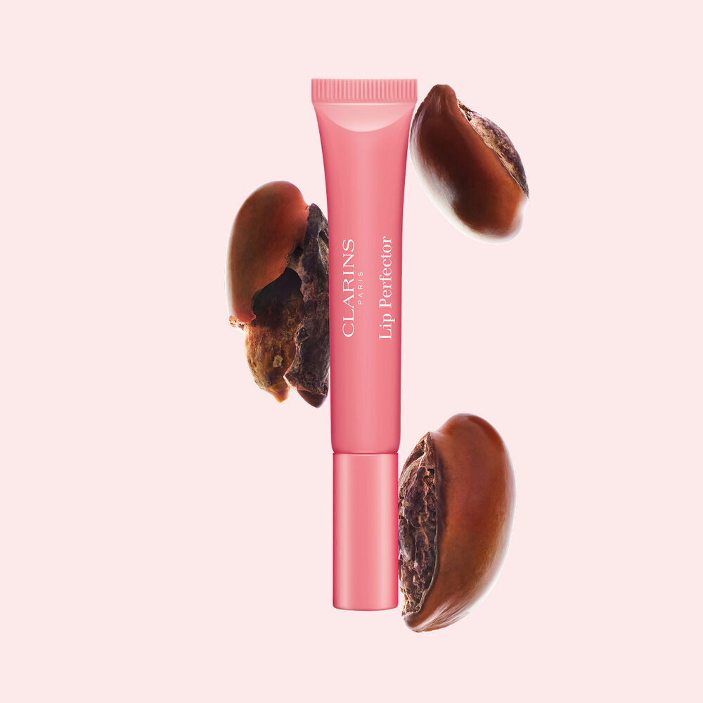 Plumping Lip Perfector junto a una semilla de karit&eacute;, destacando el karit&eacute; como ingrediente clave para unos labios nutridos y brillantes.