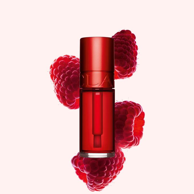 Foto del tono&nbsp;03&nbsp;rojo de Water Lip Stain de Clarins junto a dos frambuesas sobre un fondo rosa claro.