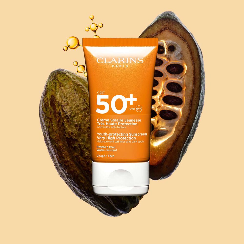 Foto del tubo naranja oscuro de crema solar SPF&nbsp;50 resistente al agua al lado de granos de cacao con un fondo naranja claro
