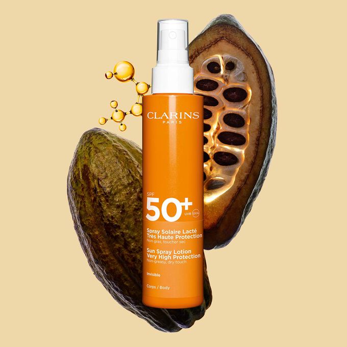 Foto del spray naranja oscuro de loci&oacute;n corporal solar SPF&nbsp;50 resistente al agua al lado de granos de cacao con un fondo naranja claro