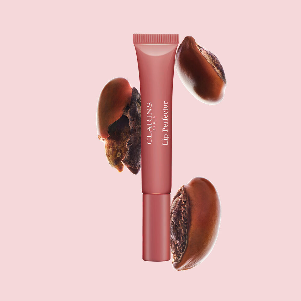Tubo de Plumping Lip Perfector mostrado con semillas de karit&eacute; crudas para resaltar la intensa f&oacute;rmula de cuidado labial con efecto nutritivo profundo.