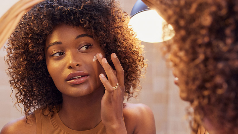 Mujer mirándose en el espejo, buscando la crema antiarrugas adecuada que se adapte a sus necesidades.