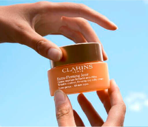 Dos manos de cerca sujetando una foto del envase de Extra Firming, cielo azul en el fondo.