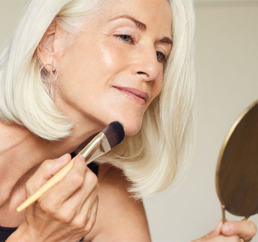 Una mujer se aplica base de maquillaje con una brocha